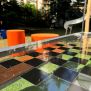 HPL Bench Chess and ludo game με επιφάνεια σκακιέρας και πορτοκαλί καθίσματα σε εξωτερικό χώρο παιχνιδιού.